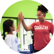 A cheerful KidStrong student high-fiving an encouraging KidStrong coach with smiles of accomplishment.